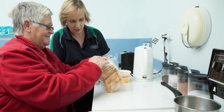Allied health staff helping an older woman in the kitchen