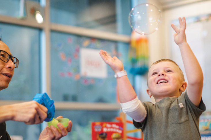 Child playing with bubbles sitting next to a man