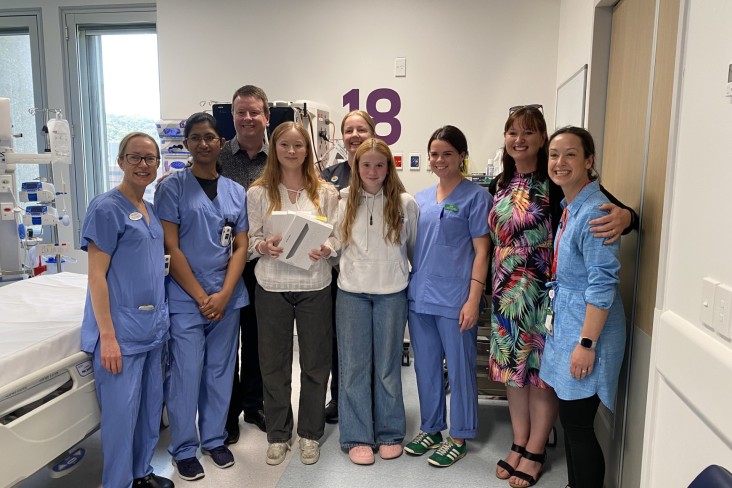 A group of staff and family stand in ICU with three electronic tablets