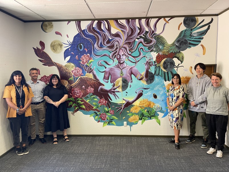 Staff and supporting stakeholders stand beside a new mural in the YSS building in Dunedin.